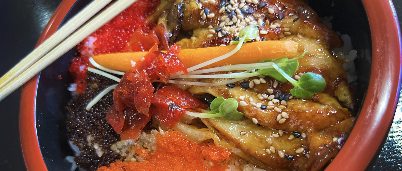 The unagi donburi is presented beautifully with colorful sections of eel, tobiko, and masago placed over subtly seasoned rice.