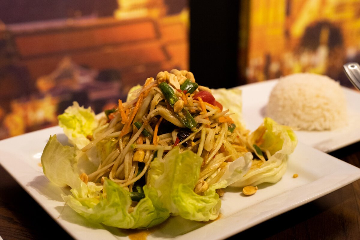 The papaya salad (som tum gai tod) has a slaw-like texture with shredded papaya and vegetables, topped with crunchy peanuts.