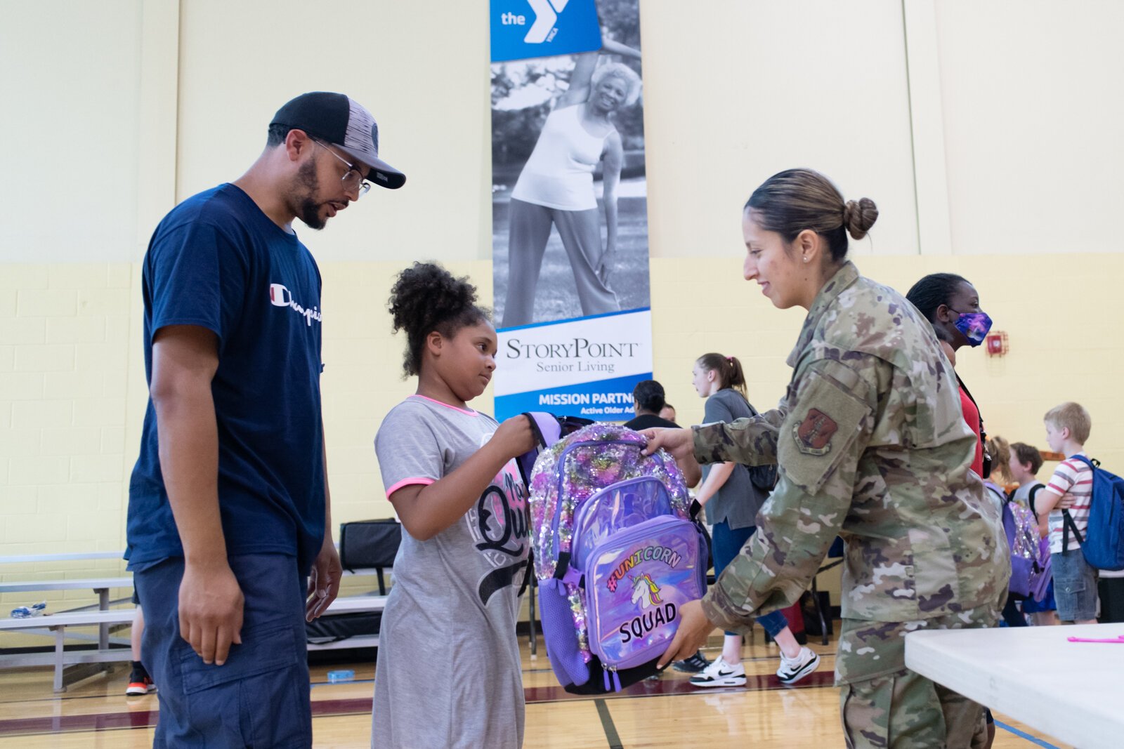 From right: Valeria Aguilar with the US Air Force hands a book bag to Serenity, 9, as her father Quenten Price looks on during the Book Bag Giveaway at Renaissance Pointe YMCA, 2323 Bowser Ave.