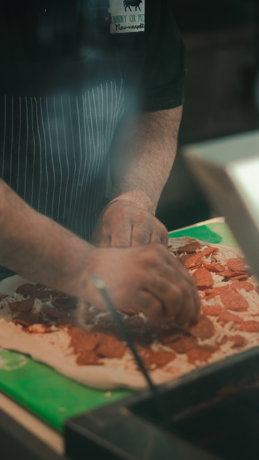 Johnny Bojinoff places toppings on a pizza.