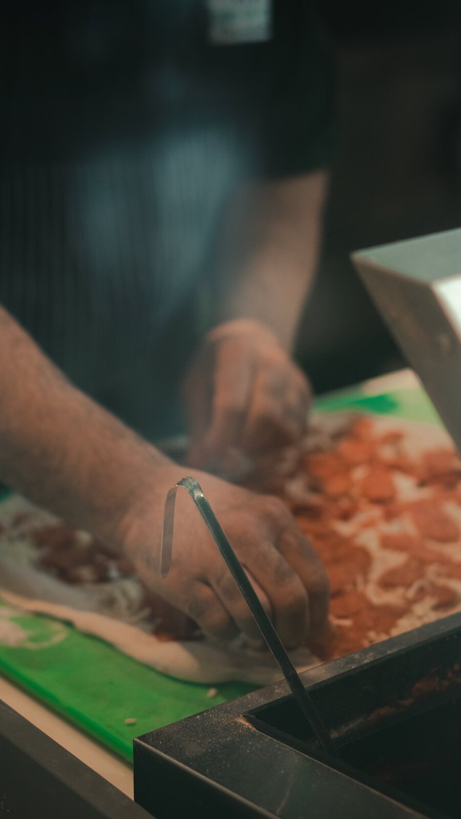 Johnny Bojinoff places toppings on a pizza.