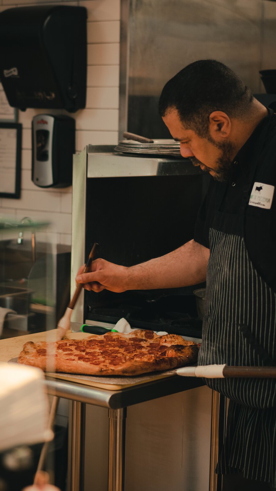 Owner of Johnny OX Pizzeria, Johnny Bojinoff, brushes a freshly made pizza.