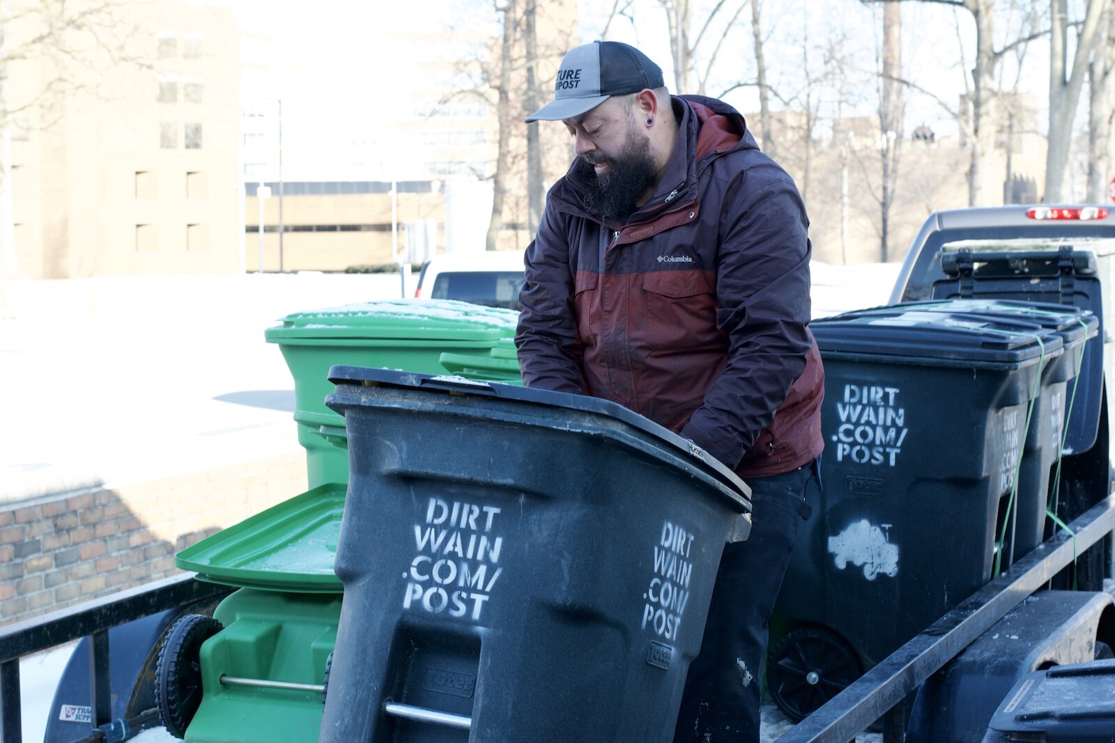 Dirt Wain’s Founder Brett Bloom loads compost bins into a pickup truck.
