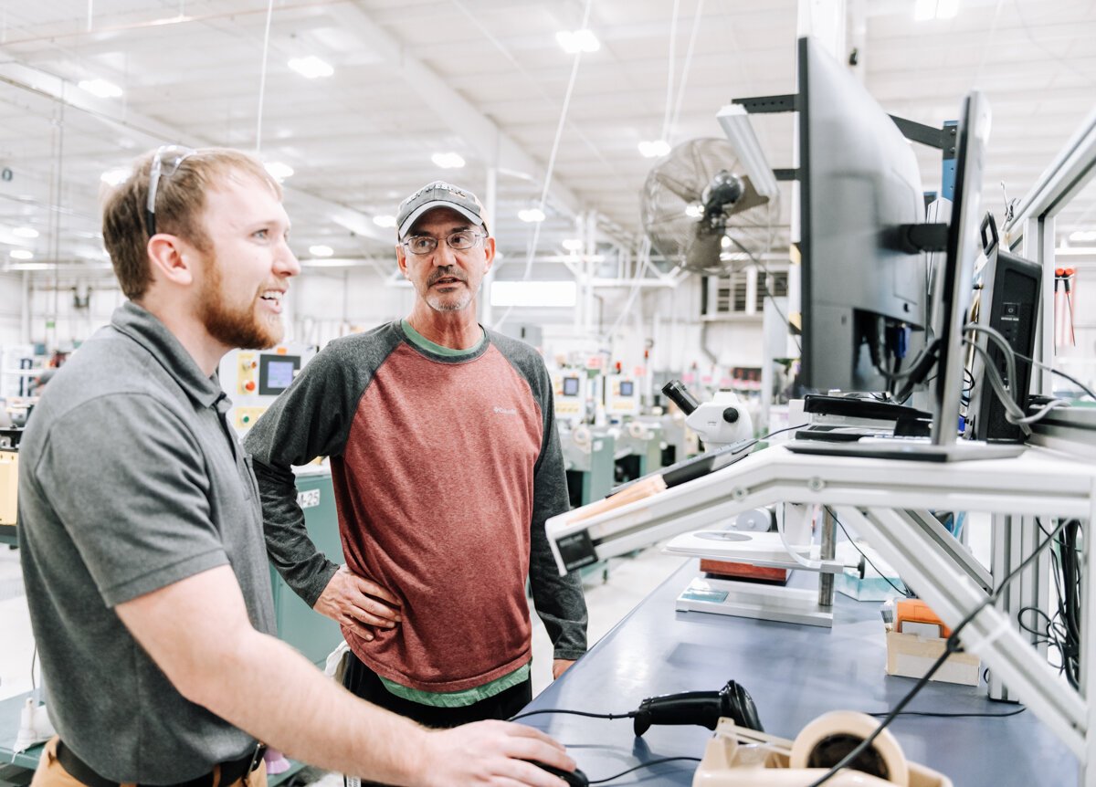 Blake Nicol, left, Senior Process Engineer works with Brad Peffley, Wire Drawer, using new technology that provides real time & historical data via a web interface that collects data from 70-80 machines in the one building in the Avionics Building.