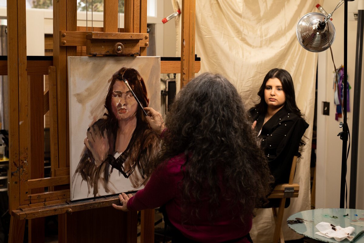 Hilarie Couture, left, paints Malak El-Taleb of Libyan heritage, right, in her home studio for her exhibit Unity with Variety.