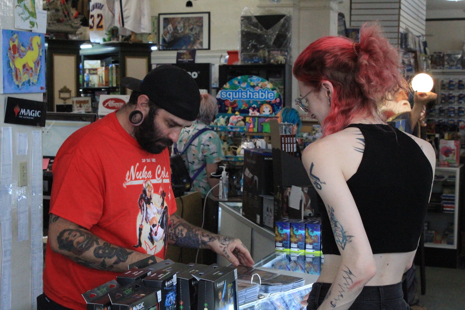 A customers looks through a binder of cards with a TCB Games employee.
