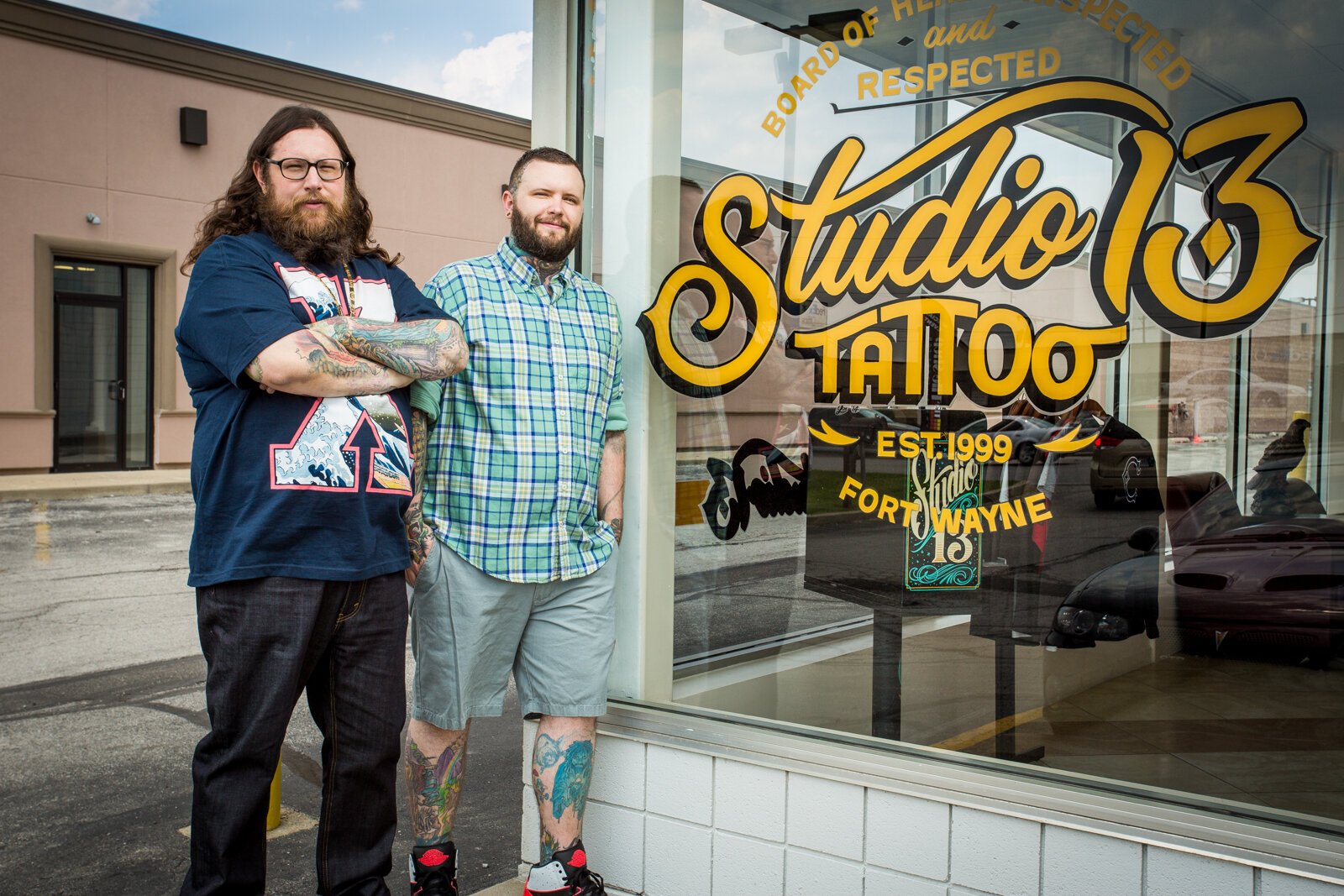 Portrait of Studio 13 owners Jake, left, and brother Jes Farris in front of a hand painted sign by Justin Lim at their Fort Wayne location on Coliseum Blvd.