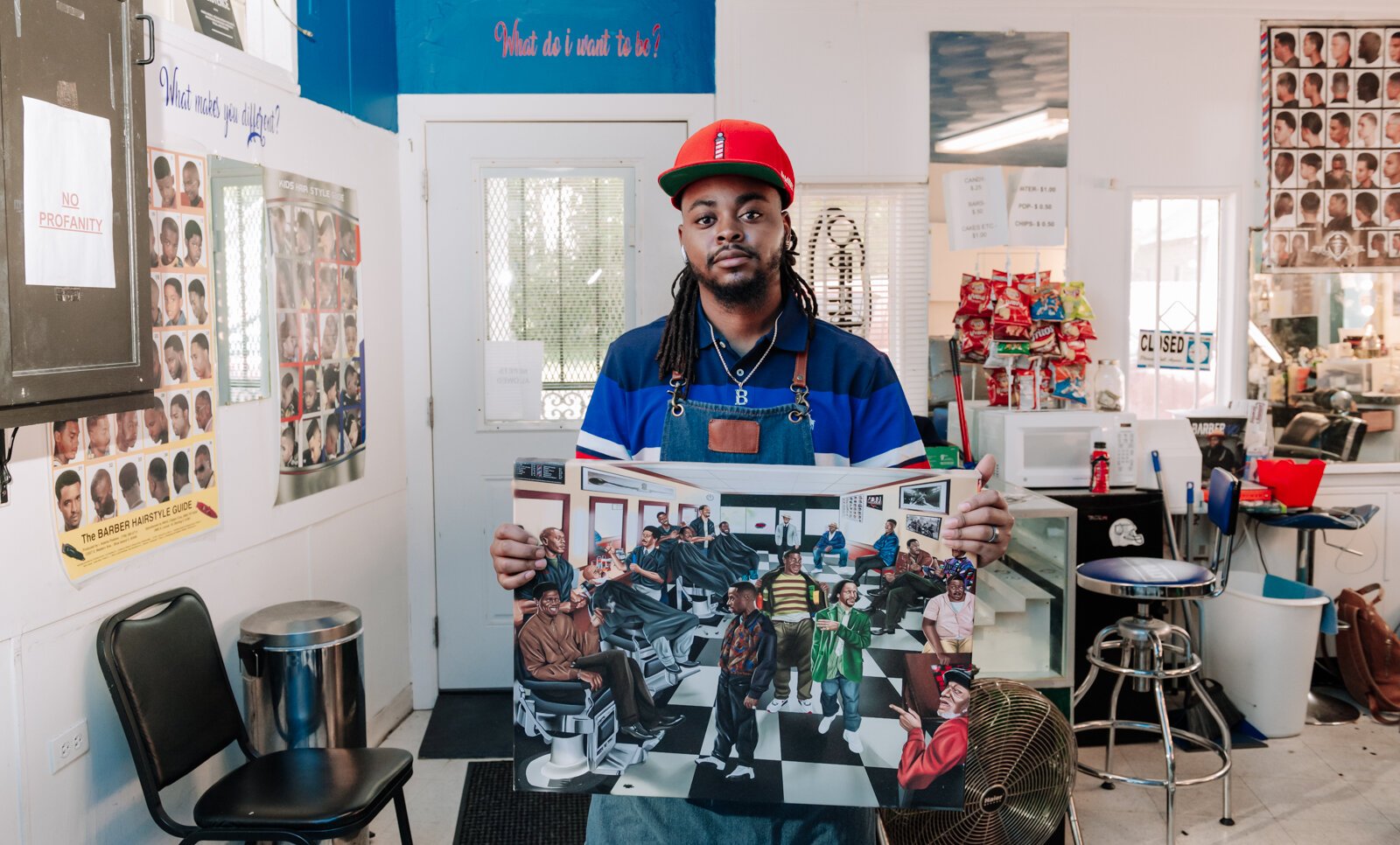 Barber Benson Harvey, owner of Smooth Kutz,  holding artwork depicting old school comedians.