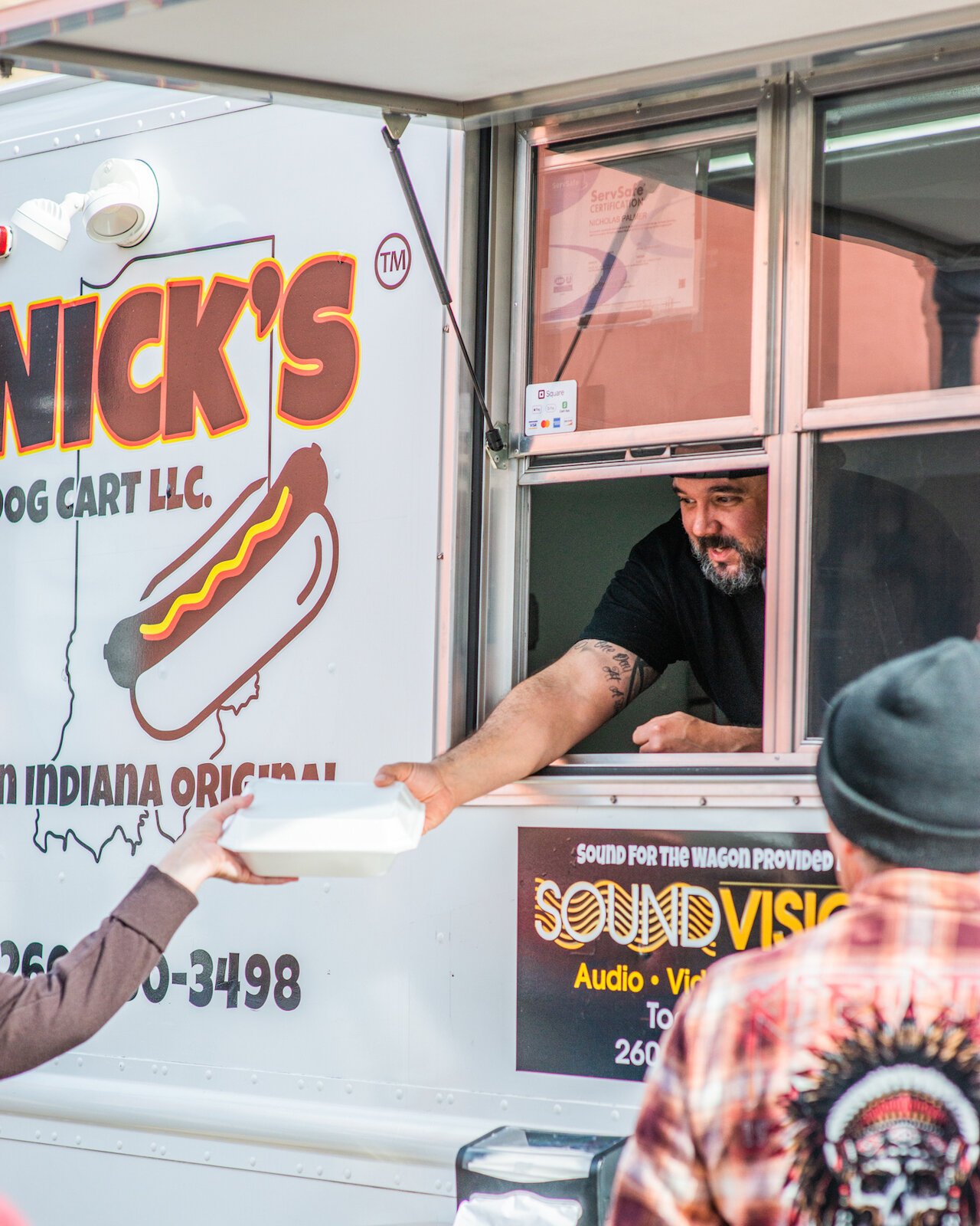 Nick Palmer, the owner of Nick's Dog Cart, hands a customer their food.