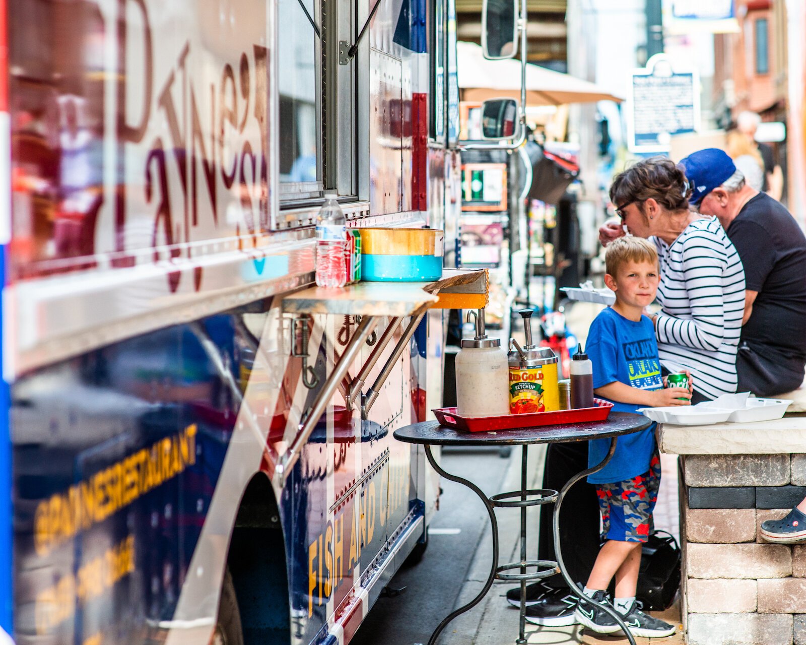 People sit along the sidewalk, enjoying food from local food trucks at First Friday in Wabash.