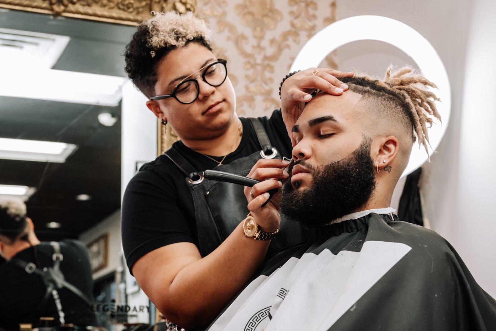 Sasha Chaney, Master Barber and Owner of Legendary Barber Lounge works on giving fellow barber Marcus Chezem a high ball fade with a beard edge up.