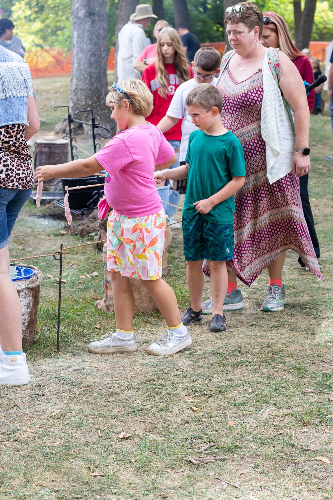 Festival attendees at a candle-making booth walk around in a circle, dipping their soon-to-be candles in wax and water repeatedly.