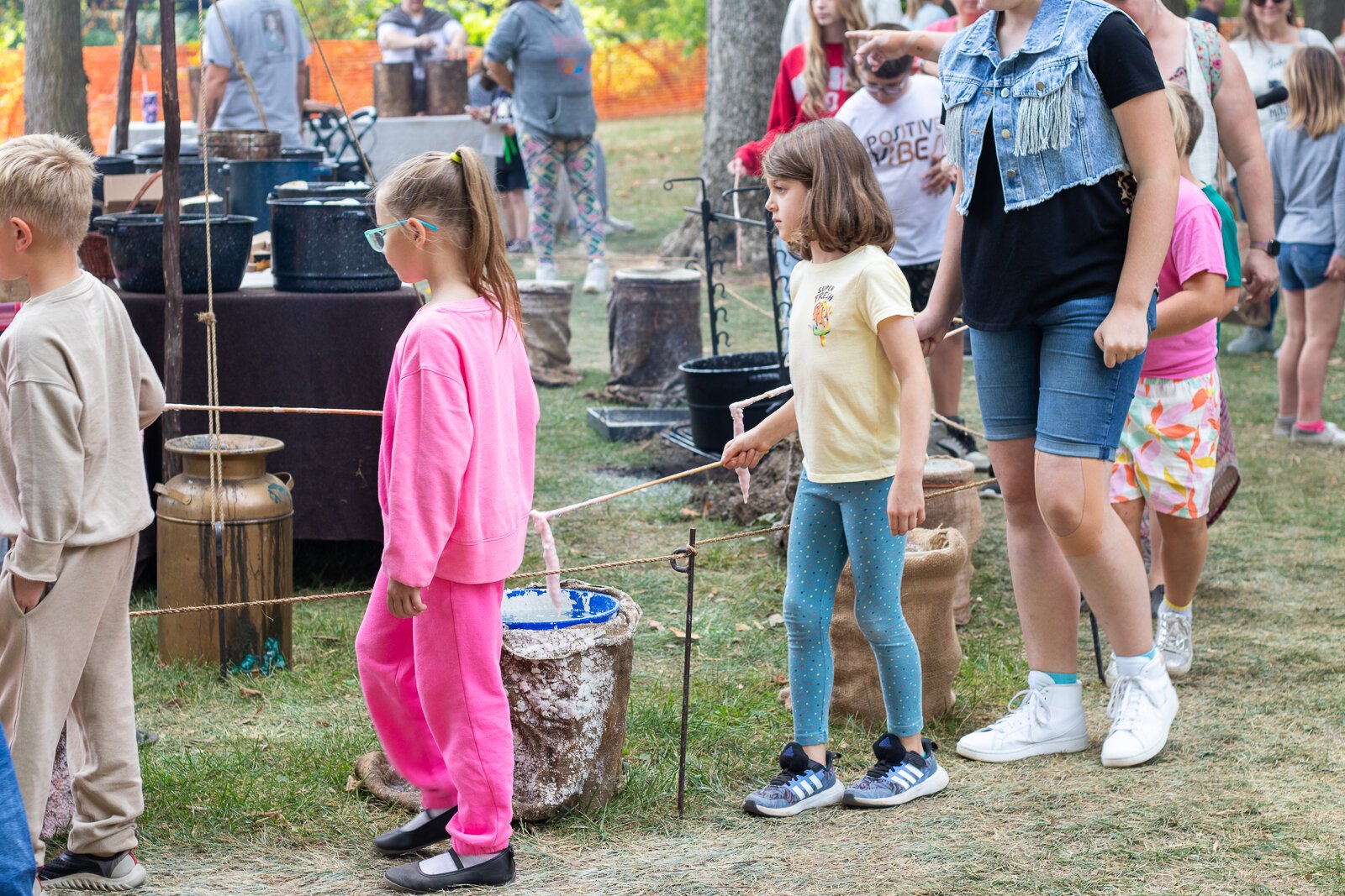 Festival attendees at a candle-making booth walk around in a circle, dipping their soon-to-be candles in wax and water repeatedly.