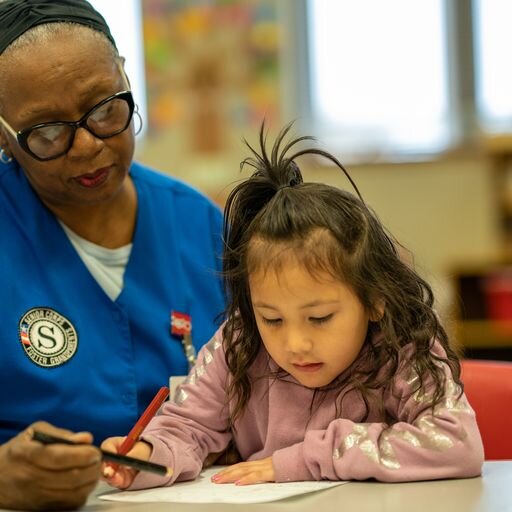 Foster Grandparent Orca helps a preschooler with their work.