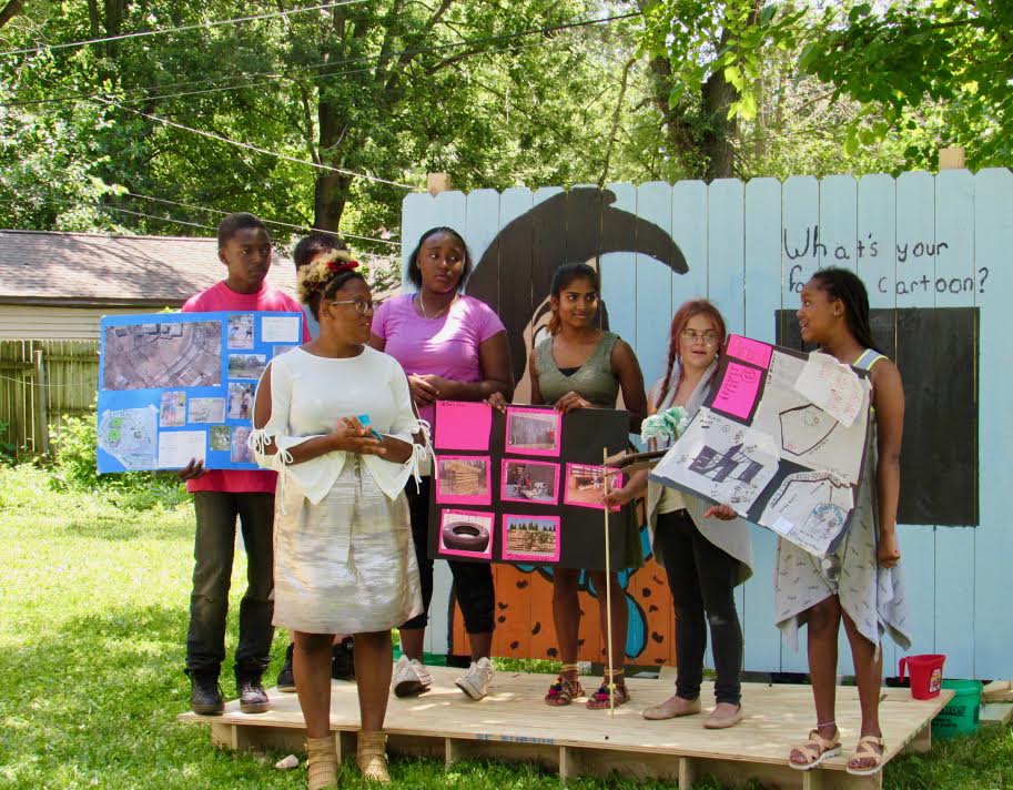 A Tired-a-Lot Summer Studio group presents their designs for a community space in front of a mural they designed and painted.