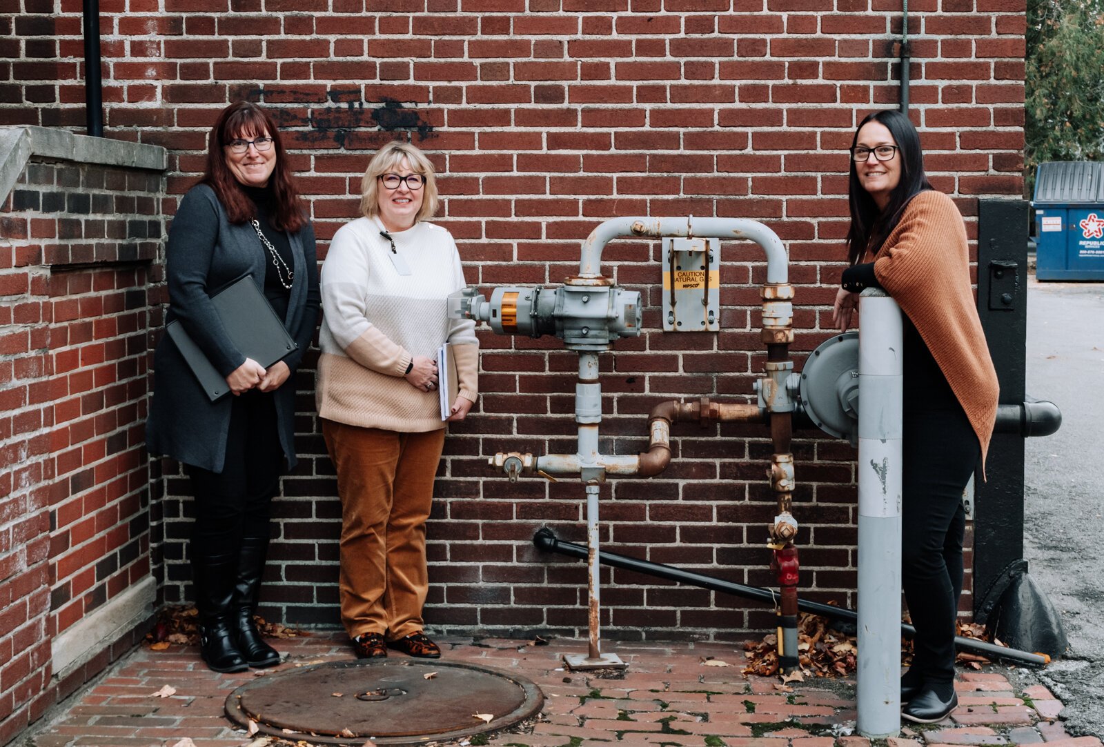 Lesa Cassel, left, Brightpoint Family Support Services Manager, Pam Brookshire, center, Brightpoint VP of Community Services, and Dana Berkes, right, Public Affairs & Economic Development Manager at NIPSCO, in front of a gas meter outside Brightpoint